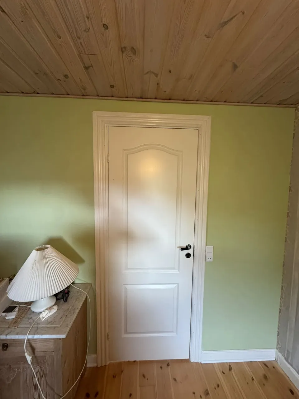Hvid dør i grøn væg med lampe i forgrunden